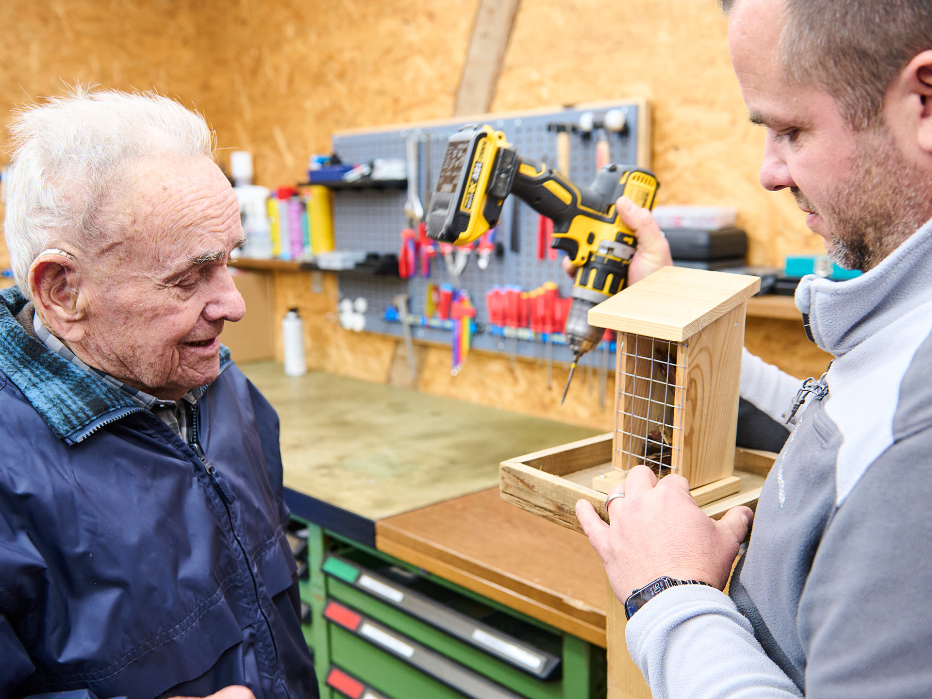 Ein Bewohner baut unter Anleitung in der Werkstatt ein Vogelhaus aus Holz.